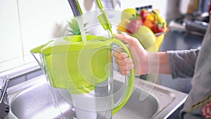 Woman filling water filter jug in the kitchen