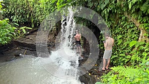 Woman filming video story of cameraman shooting a man under waterfall. Travel and make footage of tropical jungle
