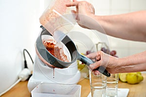 Woman filtering dark red fruits and vegetables juice with a sieve
