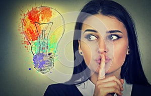 Woman with finger on lips gesture looking at bright light bulb