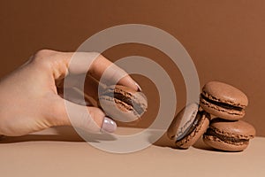 Woman fingers with brown chocolate macaroons on beige background. Sweet food. Tasty desert. Homemade meal. Delicious food. Space