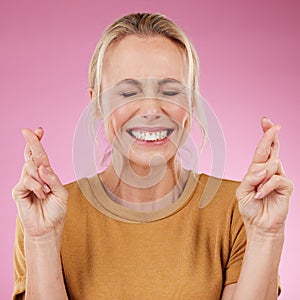 Woman, fingers crossed and hope in studio, pink background and smile face. Female model wish for luck with hands of