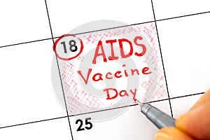 Woman fingers with pen writing reminder AIDS Vaccine Day in calendar