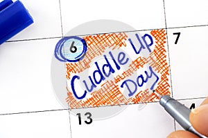 Woman fingers with pen writing reminder Cuddle Up Day in calendar