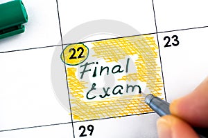 Woman fingers with pen writing reminder Final Exam in calendar