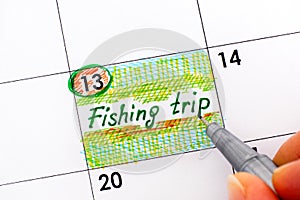 Woman fingers with pen writing reminder Fishing Trip.