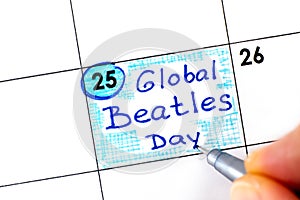 Woman fingers with pen writing reminder Global Beatles Day in calendar