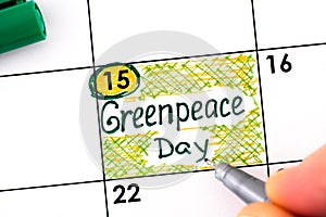 Woman fingers with pen writing reminder Greenpeace Day in calendar