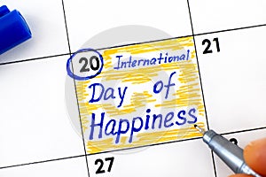 Woman fingers with pen writing reminder International Day of Happiness in calendar