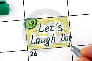 Woman fingers with pen writing reminder Lets Laugh Day in calendar