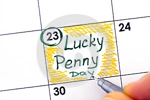 Woman fingers with pen writing reminder Lucky Penny Day in calendar