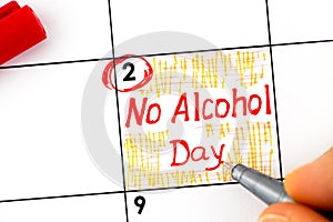 Woman fingers with pen writing reminder No Alcohol Day in calendar