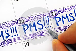 Woman fingers with pen writing reminder PMS in calendar.