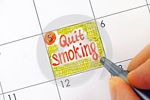 Woman fingers with pen writing reminder Quit Smoking in calendar