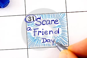 Woman fingers with pen writing reminder Scare a Friend Day in calendar