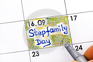 Woman fingers with pen writing reminder Stepfamily Day in calendar photo