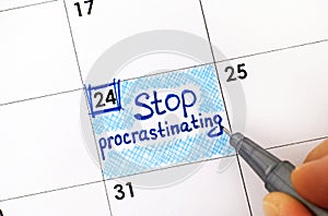 Woman fingers with pen writing reminder Stop Procrastinating in