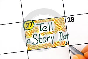 Woman fingers with pen writing reminder Tell a Story Day in calendar