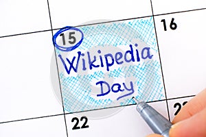 Woman fingers with pen writing reminder Wikipedia Day in calendar photo