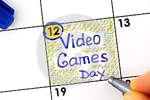 Woman fingers wirh pen writing reminder Video Games Day in calendar
