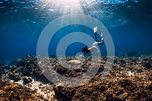 Woman with fins swimming underwater with big turtle