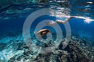 Woman with fins swimming underwater with big turtle