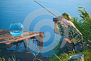 Woman fisherman carefully looks through binoculars on the river bank. Summer, hobby, vacation.