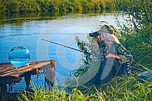 Woman fisherman carefully looks through binoculars on the river bank. Summer, hobby, vacation.