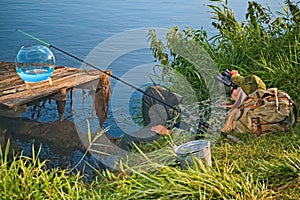 Woman fisherman is resting on a fishing trip with equipment. Lady lies in the grass and looks through binoculars.