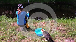 Woman fishing on lake shore and cat cath fish from bucket water
