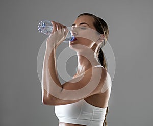 Woman, fitness and drinking with water for hydration after workout or exercise on a gray studio background. Thirsty