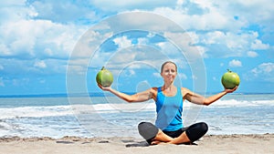 Woman fitness exercise with green coconuts on ocean beach