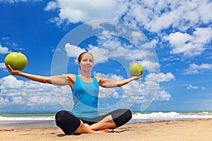 Woman fitness exercise with green coconuts on ocean beach