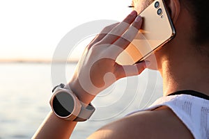 Woman with fitness tracker talking on phone near river, closeup