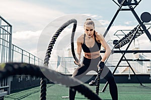 Woman in fitness wear working out with two battle ropes