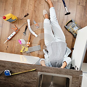 Woman fixing kitchen sink. Housewife working under kitchen