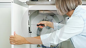 Woman fixing kitchen sink. Housewife working under kitchen sink