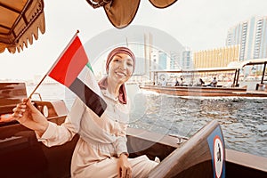 Woman with the flag of the United Arab Emirates sits in a boat during a cruise on the Dubai Creek Canal with views of