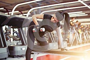 Woman flexing muscles with dumbbell on bench in gym