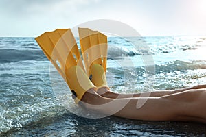 Woman in flippers near sea on beach, closeup