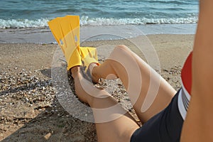 Woman in flippers sitting near sea on beach