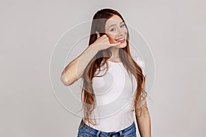 Woman flirting holding fingers near ear showing call gesture with toothy smile, answering call.