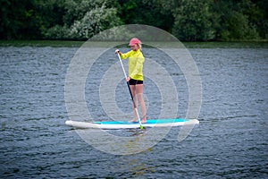 A woman is floating on a SUP board along a large river. Stand on the paddle boarding - amazing outdoor activities