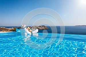 Woman floats on a infinity swimming pool with view to the Mediterranean sea in Greece