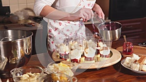Woman is flooding a fruit dessert by berries liquid marmalades in a kitchen