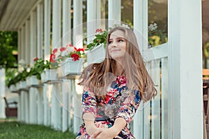 Woman in floral dress smiling near white fence with red flowers