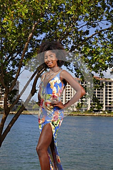 Woman in a floral pattern dress hands on hips afro and smile