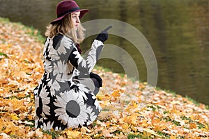 Woman in a floral patterned coat and wine red hat in the park, by the river. Happy girl, colorful autumn forest. Portrait of lady
