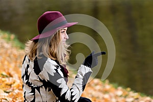 Woman in a floral patterned coat and wine red hat in the park, by the river. Happy girl, colorful autumn forest. Portrait of lady