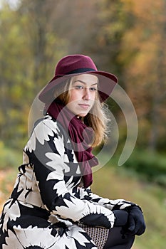 Woman in a floral patterned coat and wine red hat in the park, by the river. Happy girl, colorful autumn forest. Portrait of lady